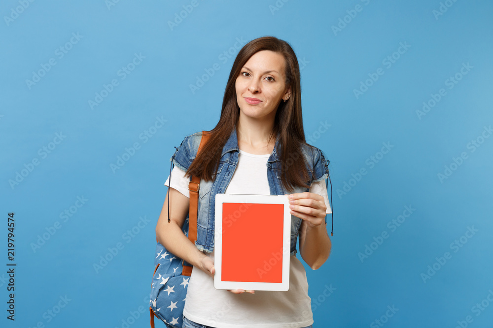 Young pretty woman student in denim clothes with backpack holding tablet pc computer with blank black empty screen isolated on blue background. Education in high school. Copy space for advertisement. Young pretty woman student in denim clothes with backpack holding tablet pc computer with blank black empty screen isolated on blue background. Education in high school. Copy space for advertisement.
