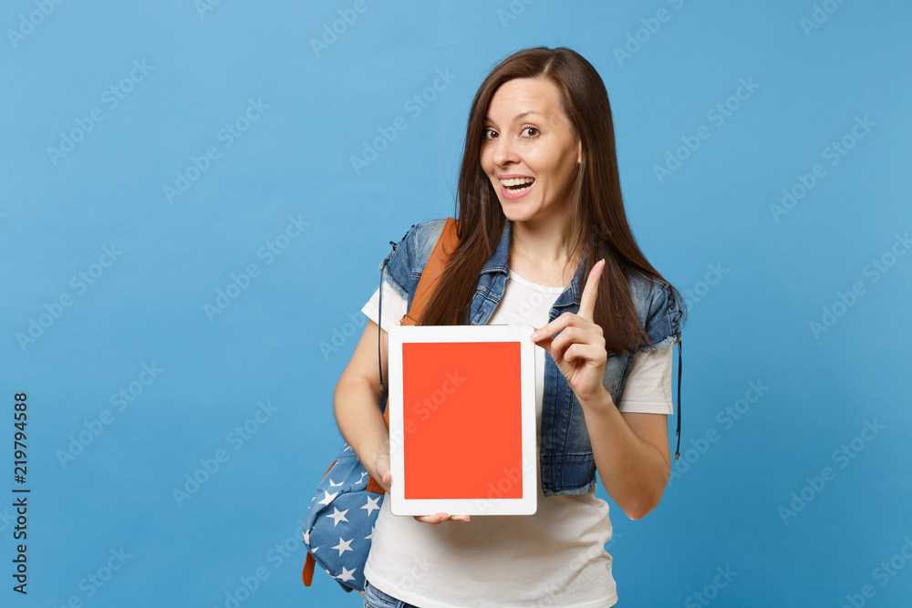 Young funny cheerful woman student pointing index finger up, holding tablet pc computer with blank black empty screen isolated on blue background. Education in college. Copy space for advertisement. Young funny cheerful woman student pointing index finger up, holding tablet pc computer with blank black empty screen isolated on blue background. Education in college. Copy space for advertisement.