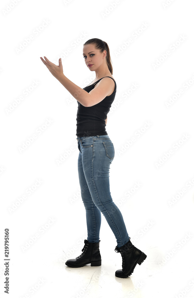 full length portrait of brunette girl wearing black single and jeans. standing pose in side profile. isolated on white studio background. full length portrait of brunette girl wearing black single and jeans. standing pose in side profile. isolated on white studio background.