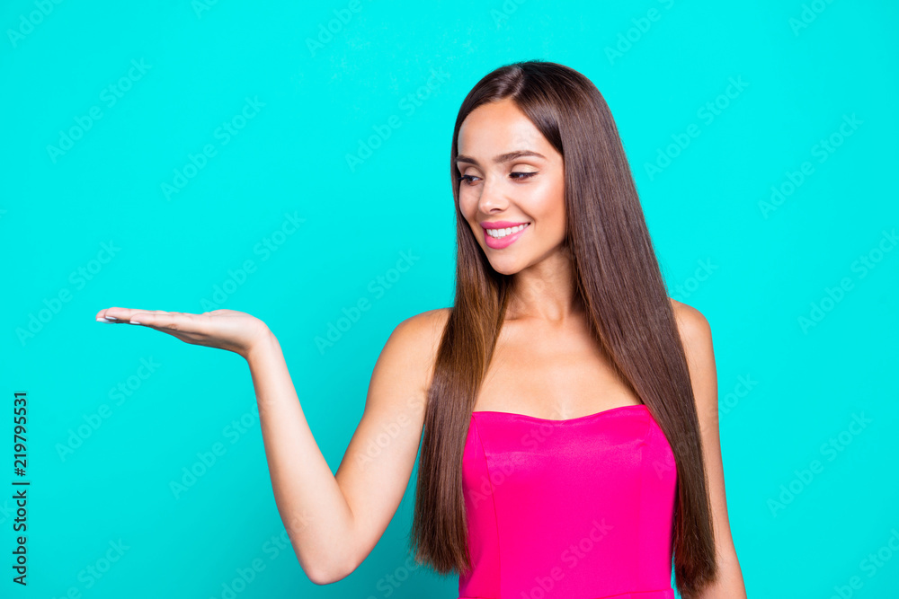 Portrait of young straight-haired long hair sweet brunette girl wearing pink top, showing object on palm. Copy space. Isolated over bright vivid teal turquoise background Portrait of young straight-haired long hair sweet brunette girl wearing pink top, showing object on palm. Copy space. Isolated over bright vivid teal turquoise background