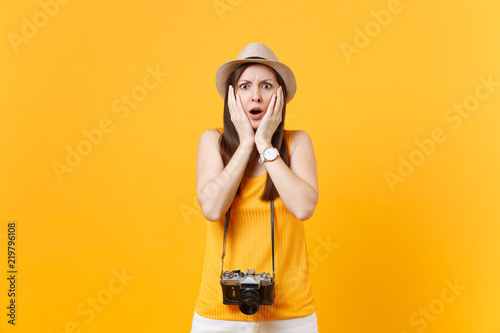 Shocked tourist woman in summer casual clothes, hat with retro vintage photo camera isolated on yellow orange background. Girl traveling abroad travel on weekends getaway. Air flight journey concept.