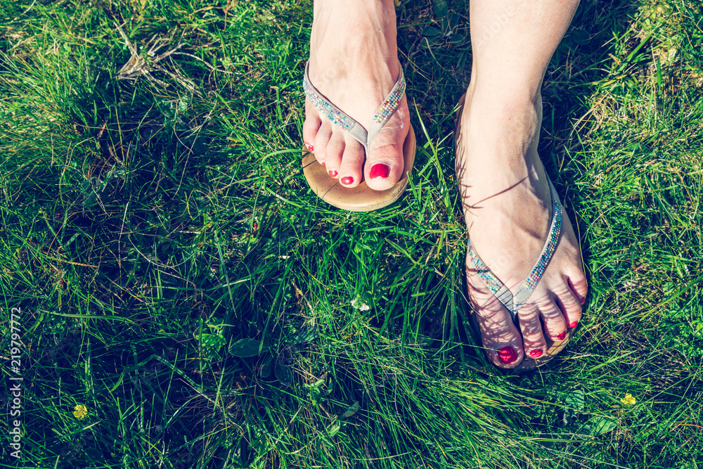 Füße eines jungen Mädchens mit Flipflops und runtem Nagellack im Gras