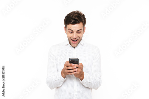 Happy young man with short dark hair chatting or typing text message with smartphone, isolated over white background © Drobot Dean