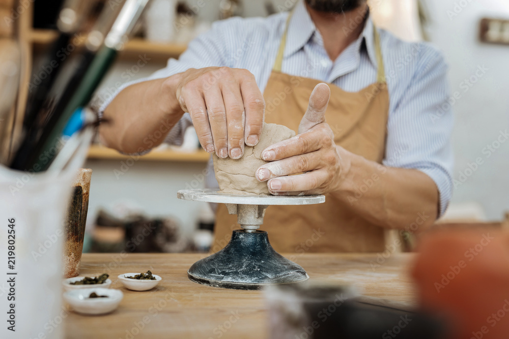 Experienced potter. Experienced professional potter wearing dark brown apron sitting near pottery wheel Experienced potter. Experienced professional potter wearing dark brown apron sitting near pottery wheel