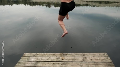 Caucasian mature man jumping from wooden pier in lake. Having fun in vacation in country side.