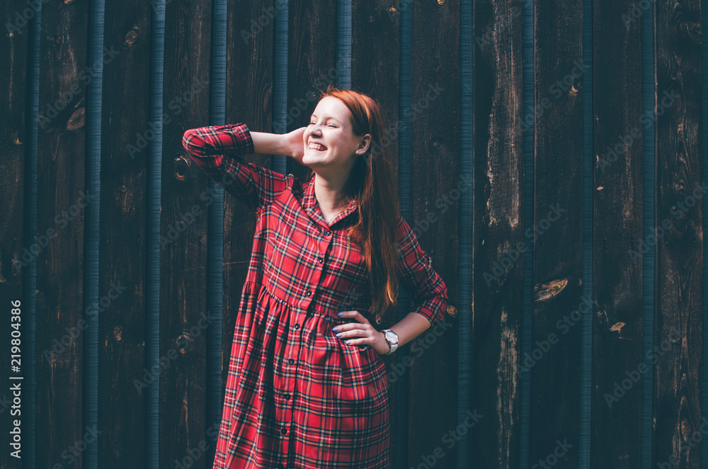 Fototapeta premium Smiling girl with long red hair standing in front of wood wall