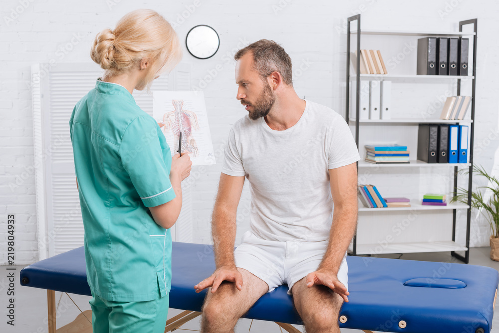 Obraz premium chiropractic showing human body picture to male patient on massage table during appointment in clinic