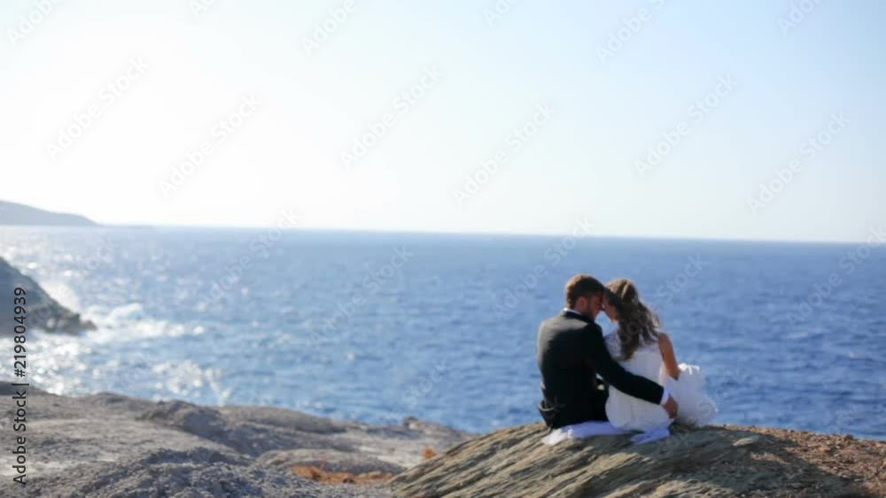 Happy bride and groom tenderly embrace on the stone shore of the sea on a sunny day. Greece Happy bride and groom tenderly embrace on the stone shore of the sea on a sunny day. Greece
