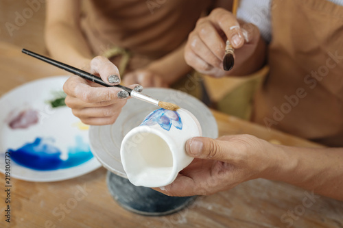 Painting flowers. Couple of creative professional artists painting some flowers on little clay pot