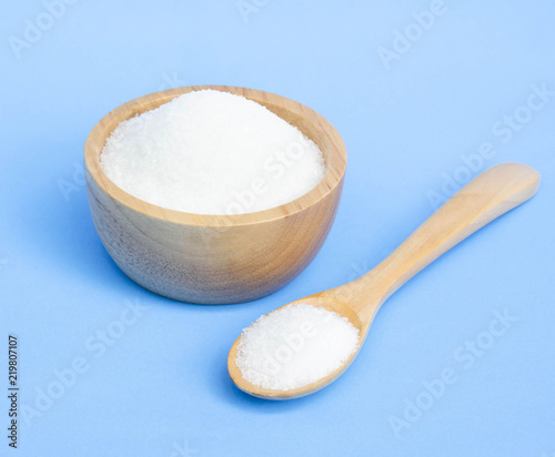 Monosodium glutamate in wood bowl and spoon on light blue background, food ingredient