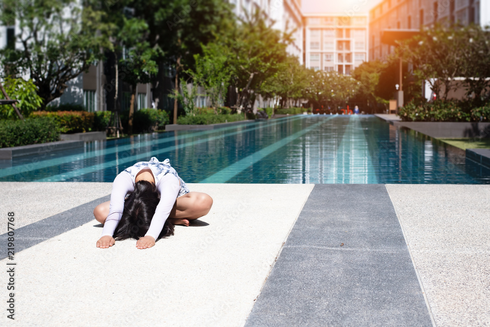 The beauty lady is sitting beside swimming pool.bend down,stretch arm and bow down,posing yoga pattern,blurry light around
