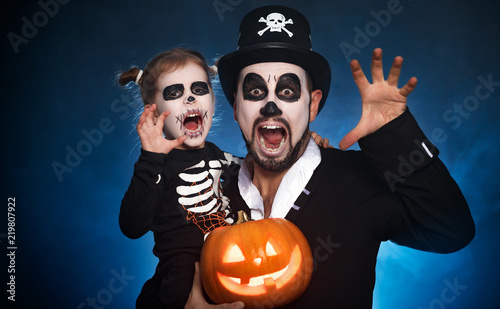 family father and daughter in costumes and make-up to Halloween with pumpkin