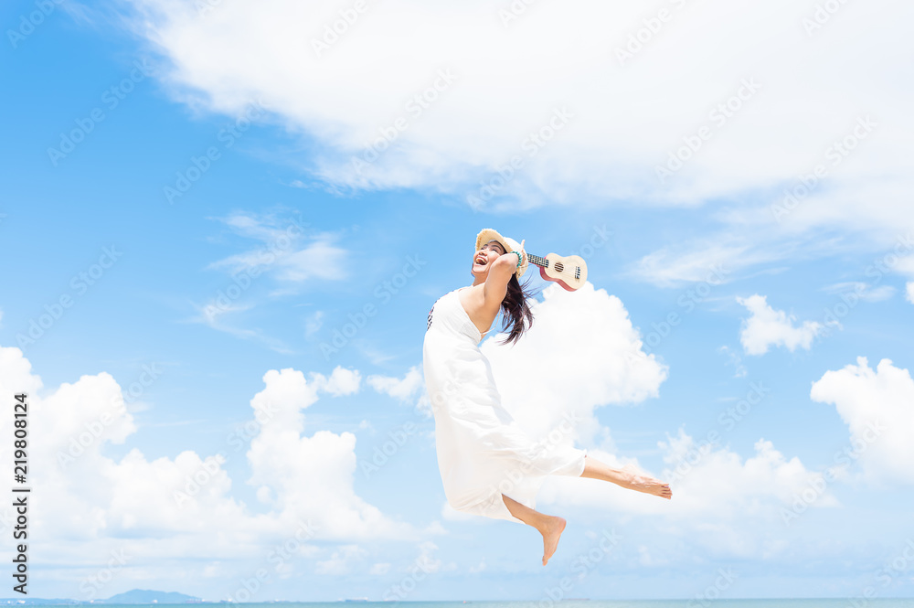 Beautiful women in white dress holding ukulele jumping along the beach. Happy women having a good mood jumping in the air. Beautiful women in white dress holding ukulele jumping along the beach. Happy women having a good mood jumping in the air.