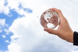 Hand Holding Glass Globe Against Sky with Clouds
