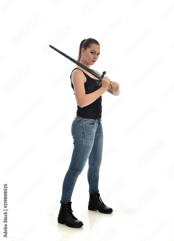 full length portrait of brunette girl wearing black single and jeans. standing pose holding a sword. isolated on white studio background. full length portrait of brunette girl wearing black single and jeans. standing pose holding a sword. isolated on white studio background.