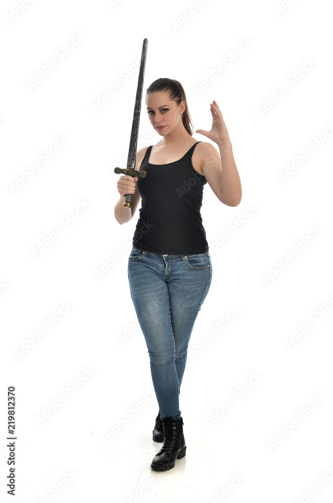 full length portrait of brunette girl wearing black single and jeans. standing pose holding a sword. isolated on white studio background. full length portrait of brunette girl wearing black single and jeans. standing pose holding a sword. isolated on white studio background.