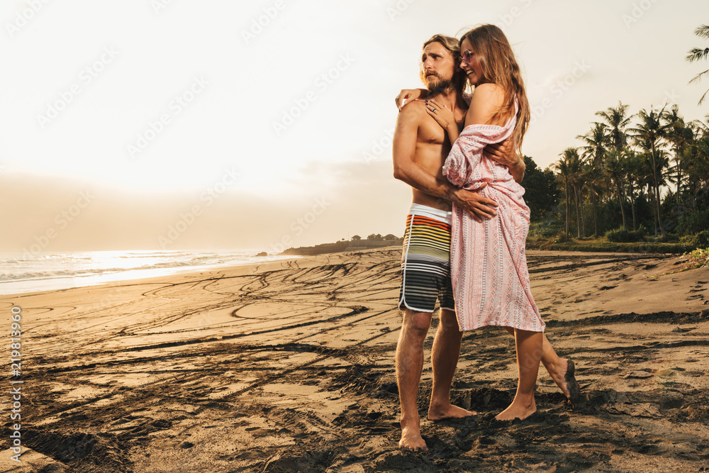 affectionate couple hugging on beach and looking away in bali, indonesia affectionate couple hugging on beach and looking away in bali, indonesia