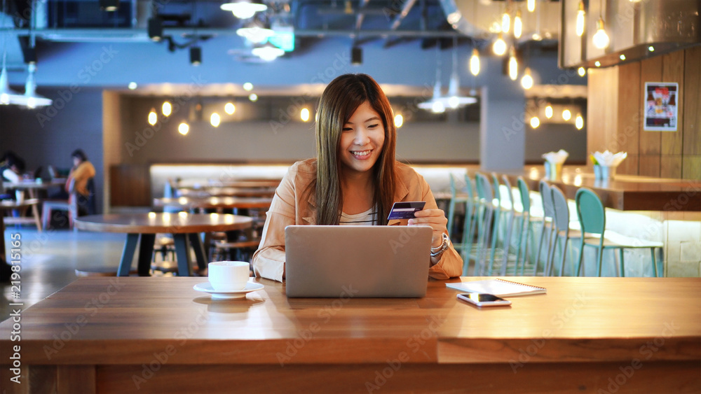 Asian businesswoman in casual suit using the credit card with computer for online shopping at co-working space, business technology and lifestyle concept