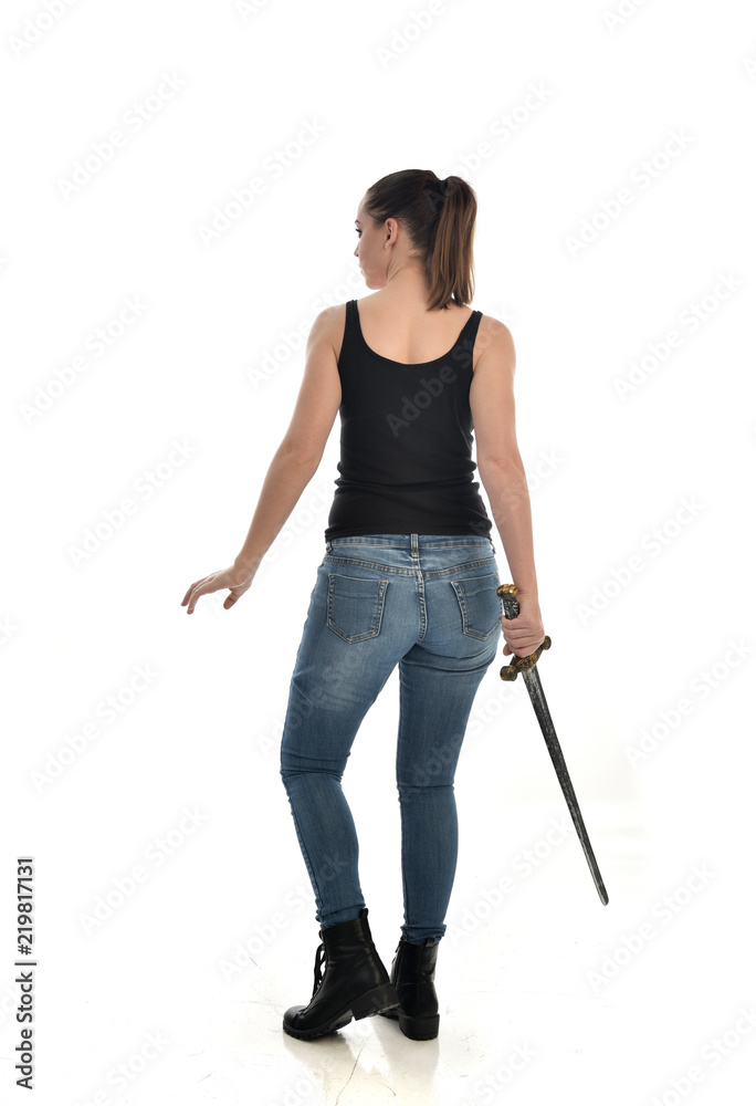 full length portrait of brunette girl wearing black single and jeans. standing pose holding a sword. isolated on white studio background. full length portrait of brunette girl wearing black single and jeans. standing pose holding a sword. isolated on white studio background.