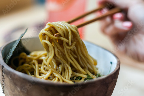 Asian traditional cuisine. Female hand pick up noodles with chopsticks. Ramen in a ceramic bowl.