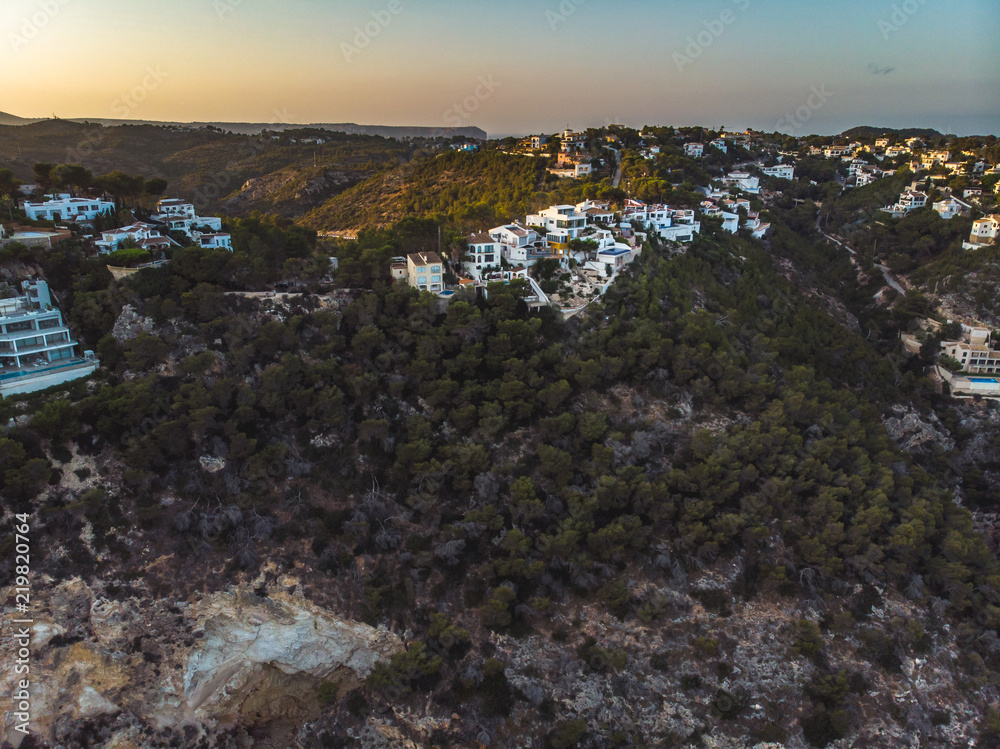 Summer 2018, Xabia, Province of Alicante, Valencia, Spain, Playa de la Granadella. Small spanish white houses on the hill surrounded and shaped by pines. Panoramic aerial photo from drone. Summer 2018, Xabia, Province of Alicante, Valencia, Spain, Playa de la Granadella. Small spanish white houses on the hill surrounded and shaped by pines. Panoramic aerial photo from drone.