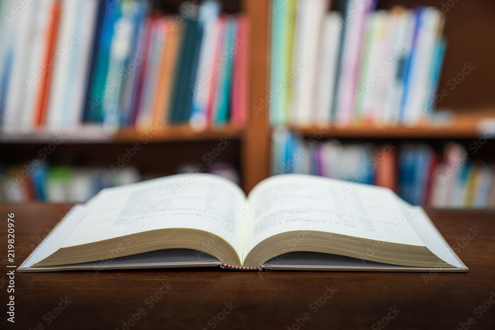 Education learning concept with opening book or textbook in old library, stack piles of literature text academic archive on reading desk and aisle of bookshelves in school study class room background