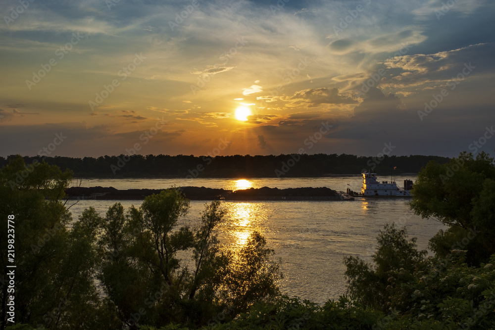 A towboat with barges in the Mississippi river at sunset near the city of Vicksburg in the State of Mississippi, USA.