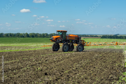 self-propelled sprayer works on a field under a blue sky with clouds