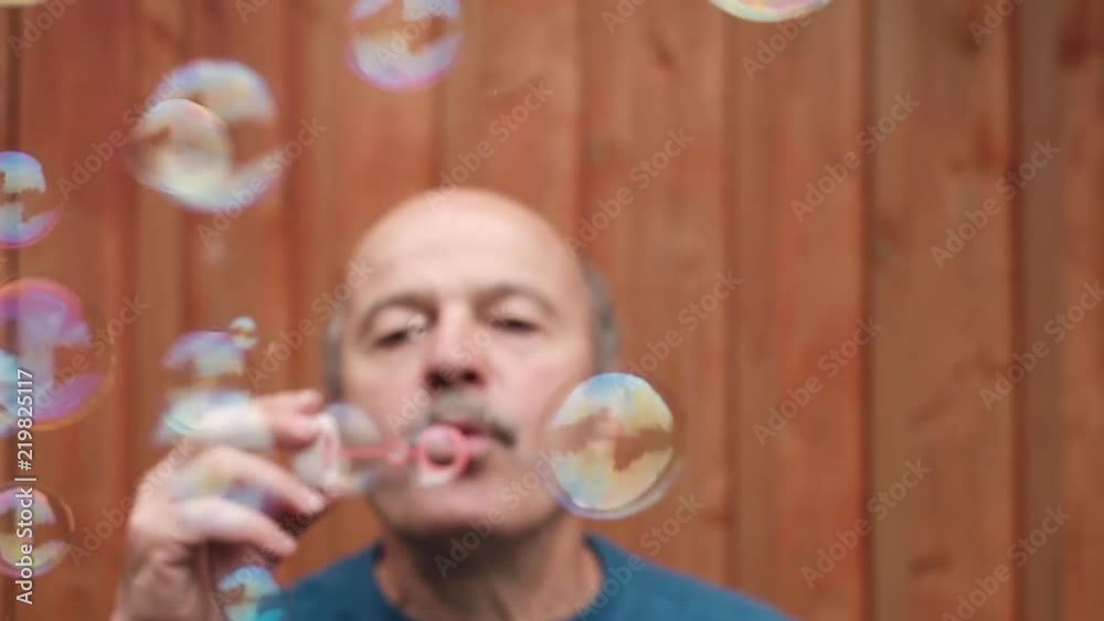 Portrait of bald caucasian senior man with mustache blowing up soap bubbles. Having a good childish mood Portrait of bald caucasian senior man with mustache blowing up soap bubbles. Having a good childish mood
