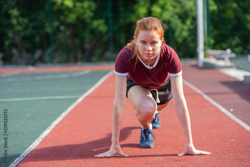 Obraz premium the red-haired student in shorts gives the standards for running for a short distance at the physical education class at an open sports ground.Female athlete ready to run on running track
