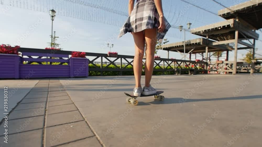 Slender girl rides a skateboard on a beautiful promenade on sunny summer evening Slender girl rides a skateboard on a beautiful promenade on sunny summer evening