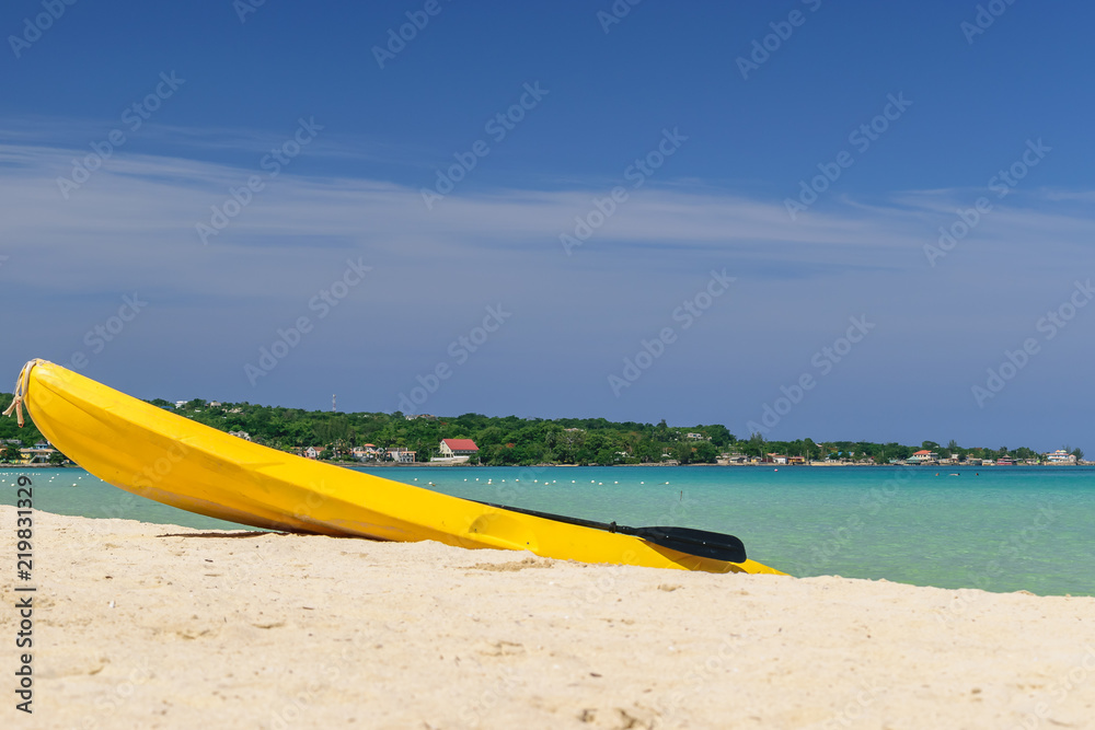 Yellow kayak and paddle by the seashore on this beautiful white sand Caribbean electric blue beach in Negril, Jamaica. No people, quiet peaceful sunny day, endless views of the turquoise ocean.