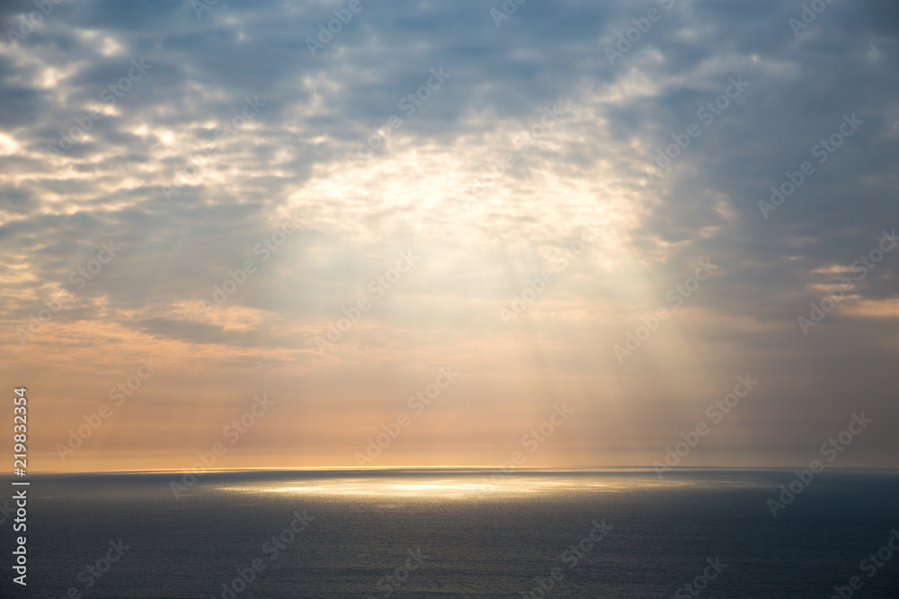 Golden light breaks through the grey sky. The sun's rays look through the clouds over the ocean.