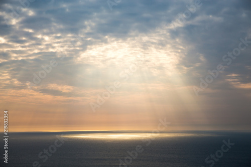 Golden light breaks through the grey sky. The sun s rays look through the clouds over the ocean.