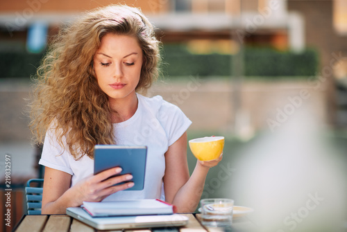 Female student using tablet and drinking coffee in cafe.