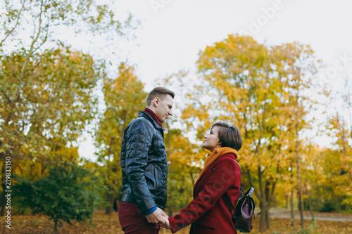 Young romantic couple in love woman and man in warm clothes holding hands looking at each other standing in autumn city park outdoors on trees background. Love relationship family people lifestyle. © ViDi Studio