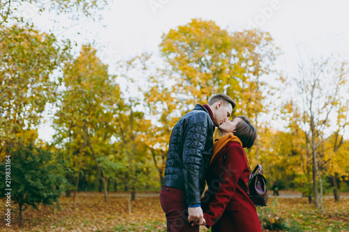 Young romantic couple in love woman and man in warm clothes holding hands kissing with closed eyes standing in autumn city park outdoors on trees background. Love relationship family people lifestyle. © ViDi Studio