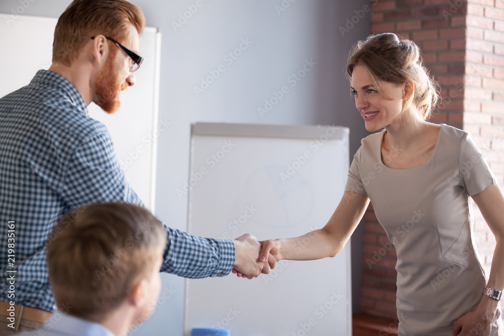 Millennial male worker shaking hand of smiling female partner or colleague during office meeting, businessman handshaking businesswoman greeting with success, employer congratulating applicant Millennial male worker shaking hand of smiling female partner or colleague during office meeting, businessman handshaking businesswoman greeting with success, employer congratulating applicant