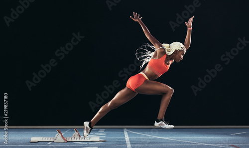 Woman athlete taking off from starting block on a running track