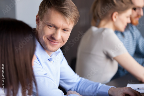 Smiling millennial man look at female colleague while working together in office, interested male employee listen attentively to woman coworker, engaged in teambuilding activity. Cooperation concept