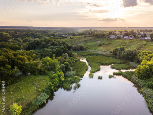 Beautiful countryside landscape with village  forest  fields  river against summer cloudy sky at sunset.