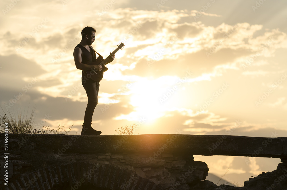 Man performs on electric guitar on old Roman aqueduct during sunset. Man performs on electric guitar on old Roman aqueduct during sunset.