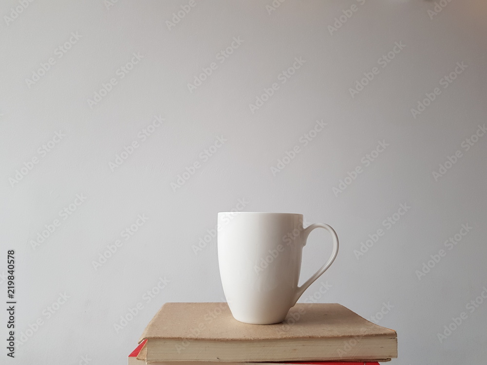Biały kubek na białym tle, stojący na stercie książek - obrazy, fototapety, plakaty 
