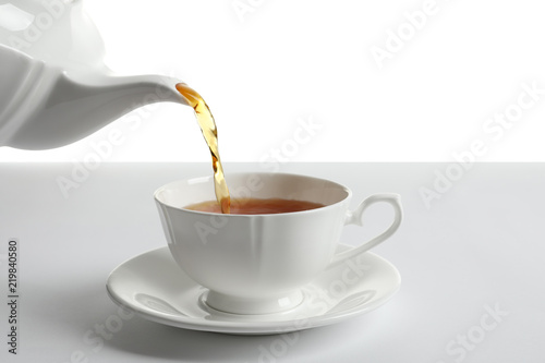 Pouring hot tea into porcelain cup on white background