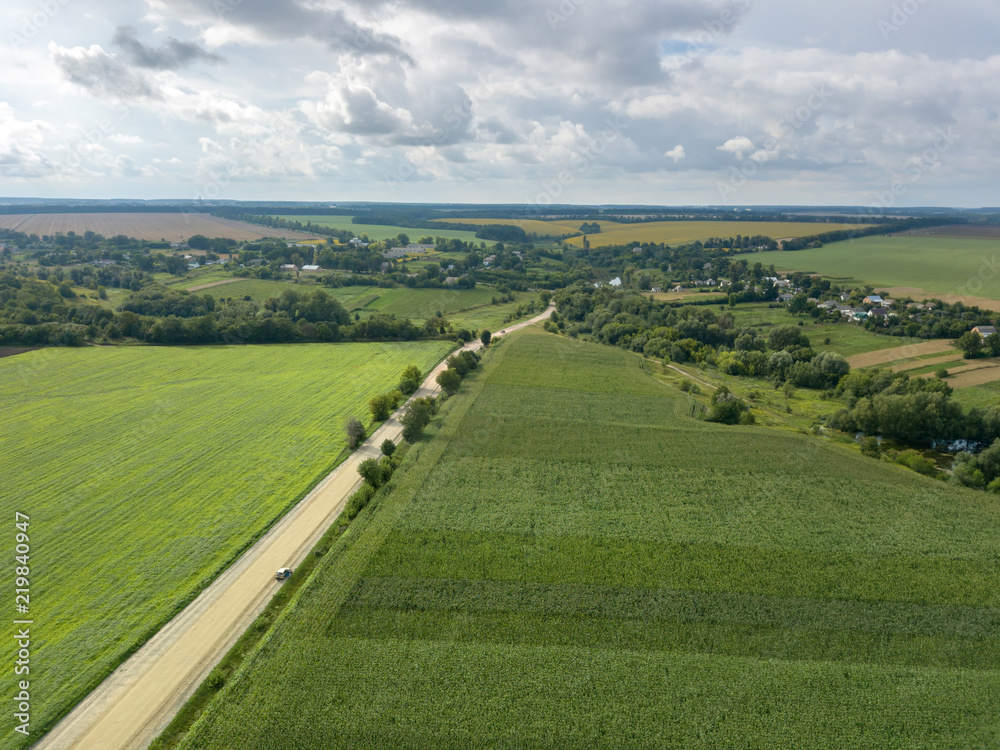 Bird's eye view from drone to a rural landscape with a village, dirt road and agricultural fields of planted crops at cloude background. Bird's eye view from drone to a rural landscape with a village, dirt road and agricultural fields of planted crops at cloude background.