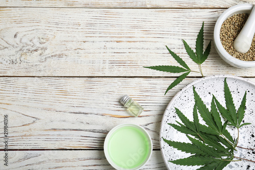 Flat lay composition with hemp leaves, seeds, cosmetic products and space for text on wooden background