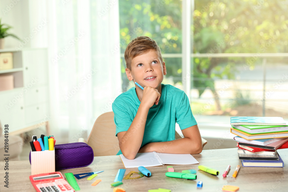 Cute boy doing homework at table with school stationery indoors Cute boy doing homework at table with school stationery indoors