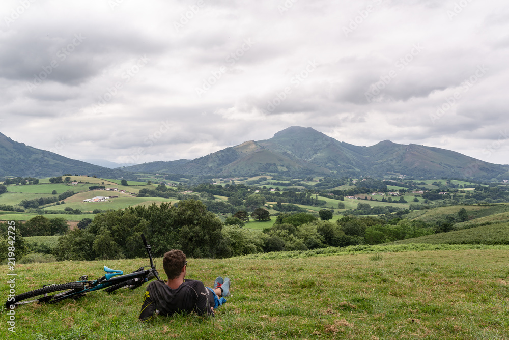 Ciclista tumbado, descansando en lo alto de una colina verde y mirando a un bonito paisaje montañoso. Pirineos, España.