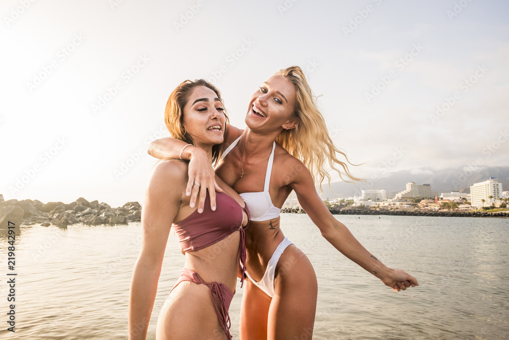 couple of thin sexy babes young woman blonde and brunette enjoy the summer  vacation hugging and laughing together. playful activity for beautiful  females and sunset backlight in background Stock Photo | Adobe