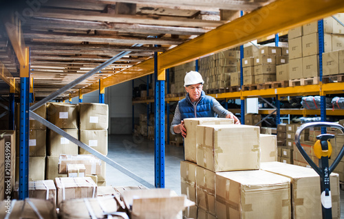 Photography Senior male warehouse worker unloading boxes from a pallet truck.